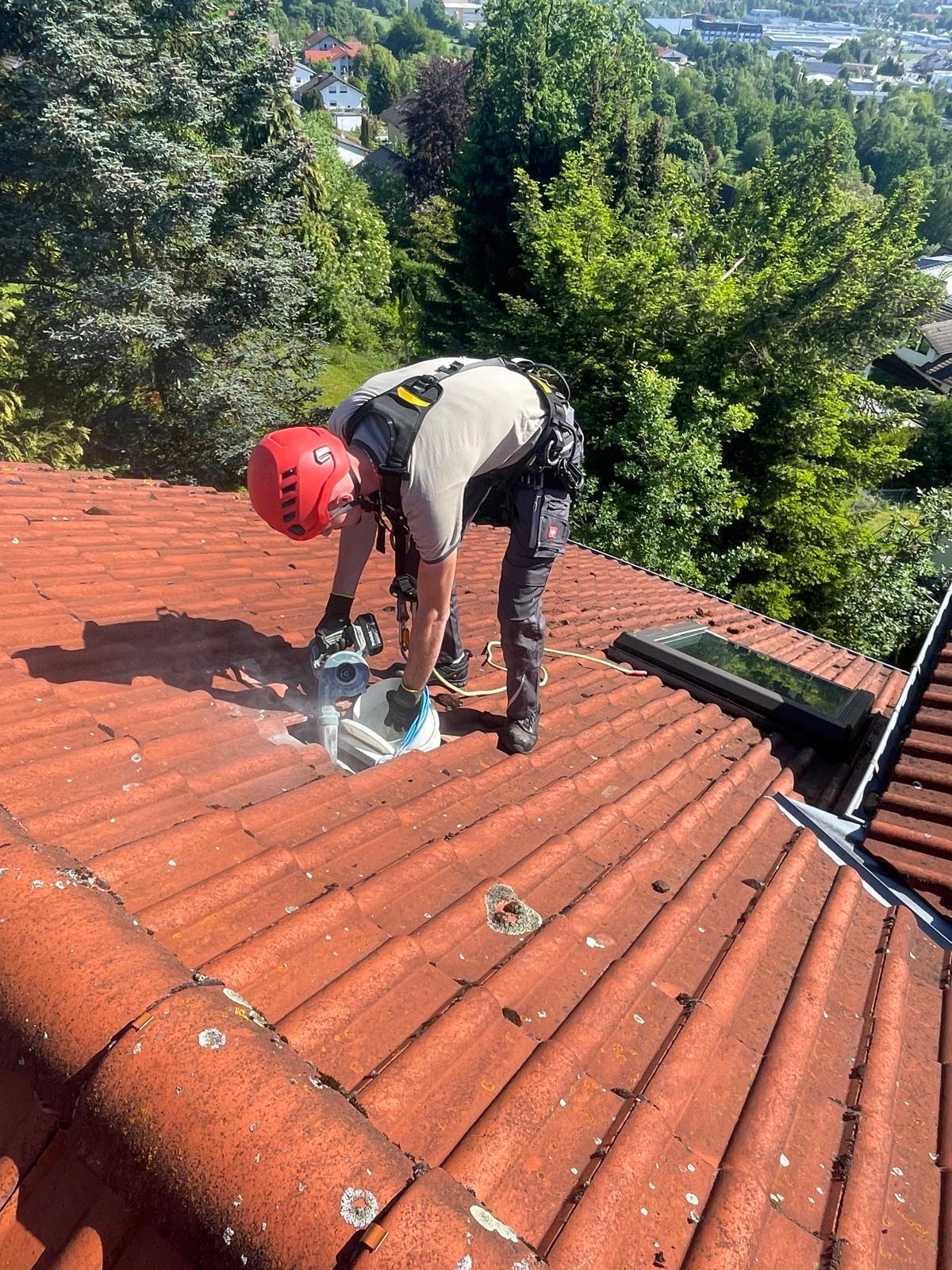 Mitarbeiter mit Helm und Sicherung bei Arbeiten auf einem Ziegeldach