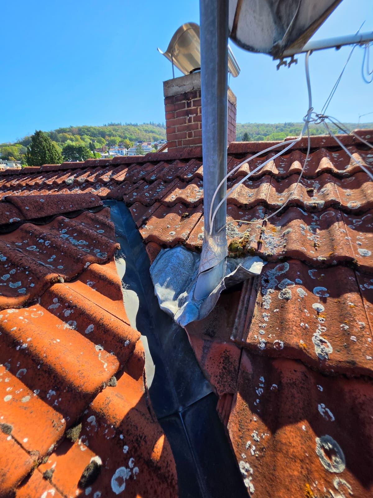 Aufgerissenes Anschlussblech an einem Rohr im Dach neben dem Schornstein